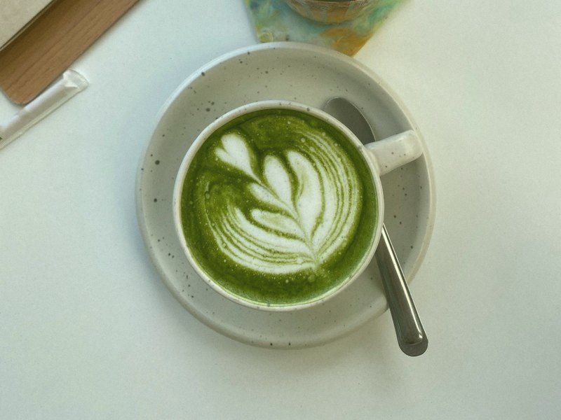 A cup of matcha latte with latte art on a white saucer, seen from above, with the matcha filter