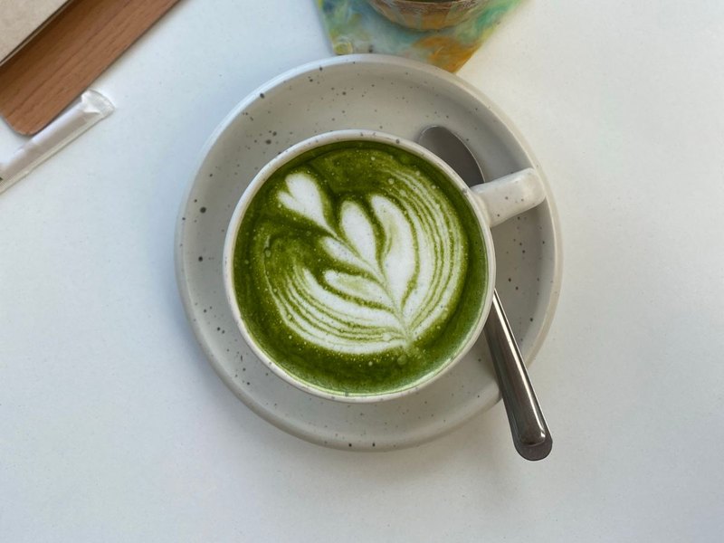 A cup of matcha latte with latte art on a white saucer, seen from above, original