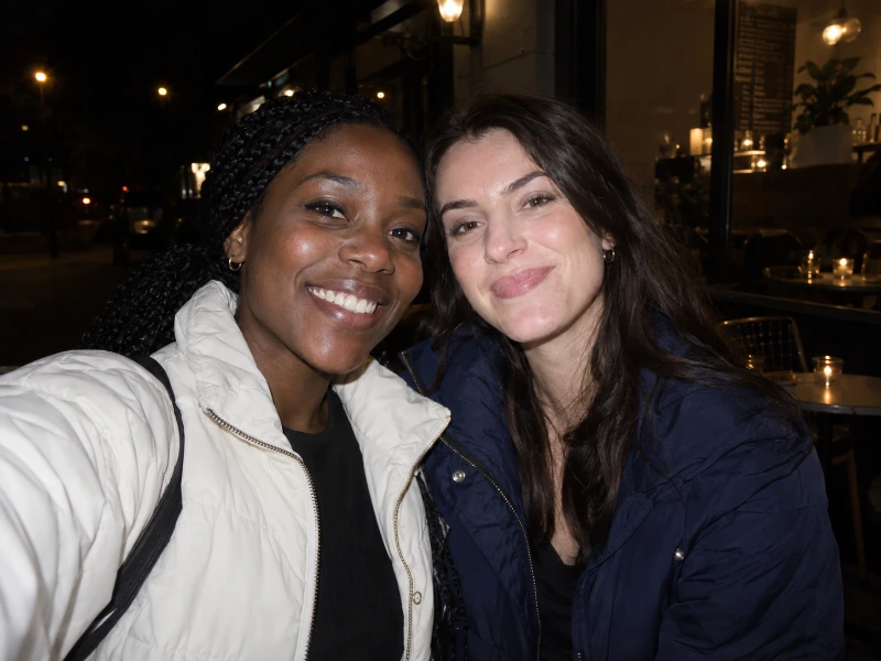 Generated direct-flash photograph of two friends outside a cafe at night — ungraded source